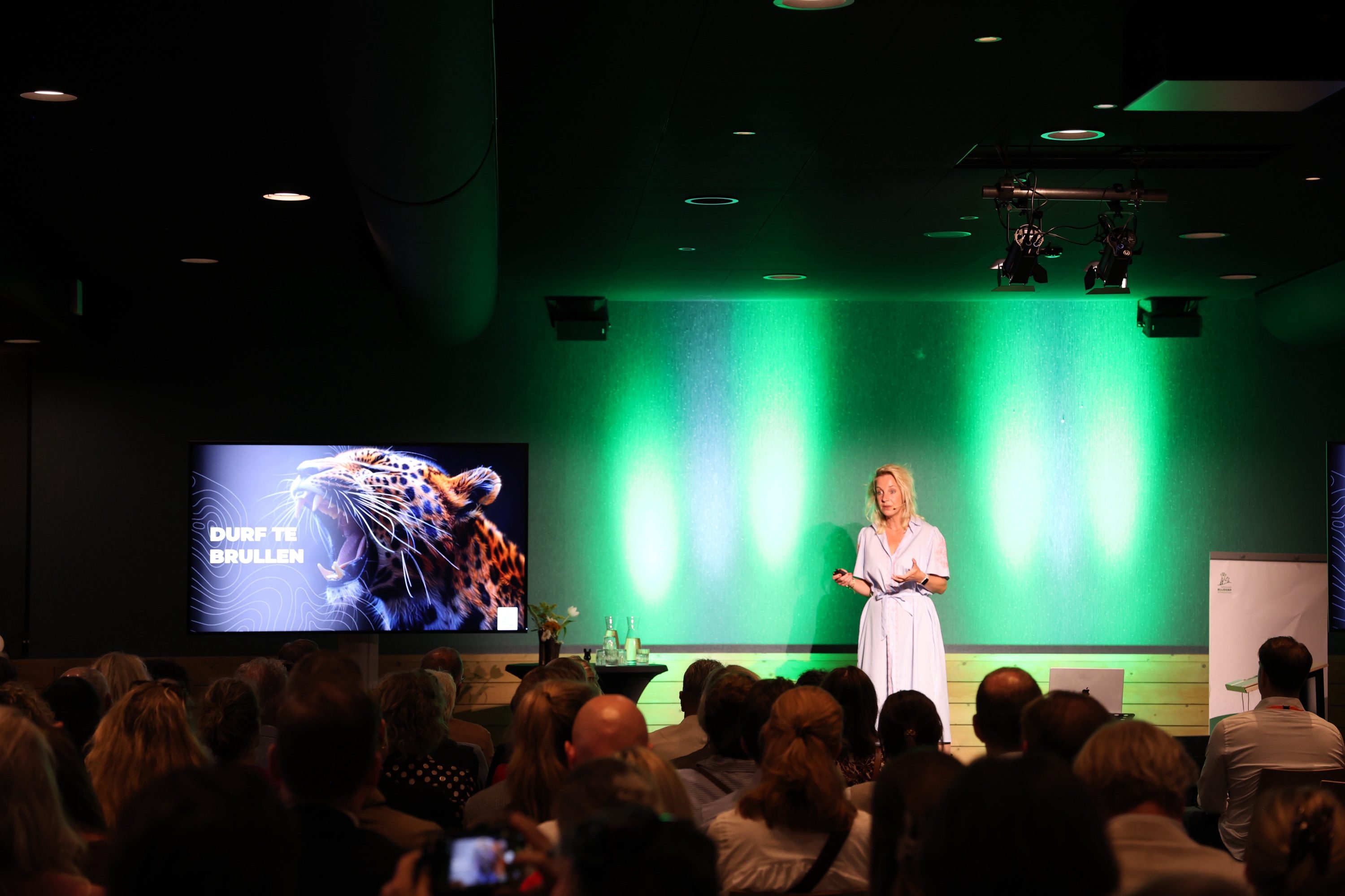Carolien Ottjes geeft een keynote voor een volle zaal, met op het scherm een brullende luipaard en de tekst Durf te brullen.